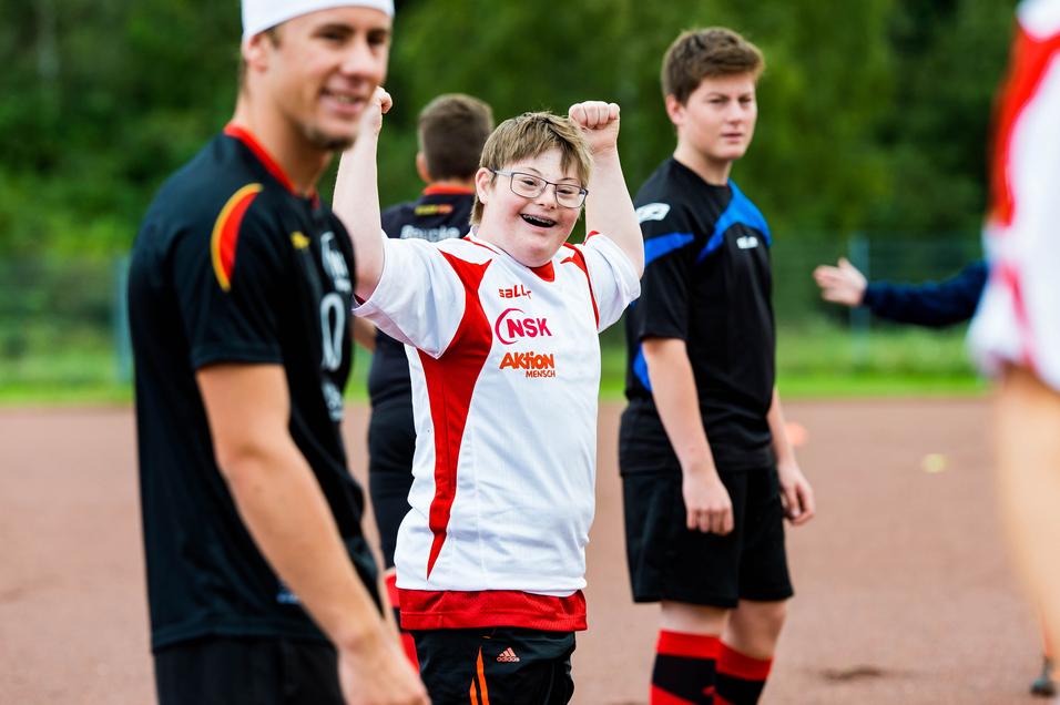 Ein junger Spieler in einem weißen Trikot hebt die Arme jubelnd, umgeben von weiteren Fußballspielern auf dem Platz.